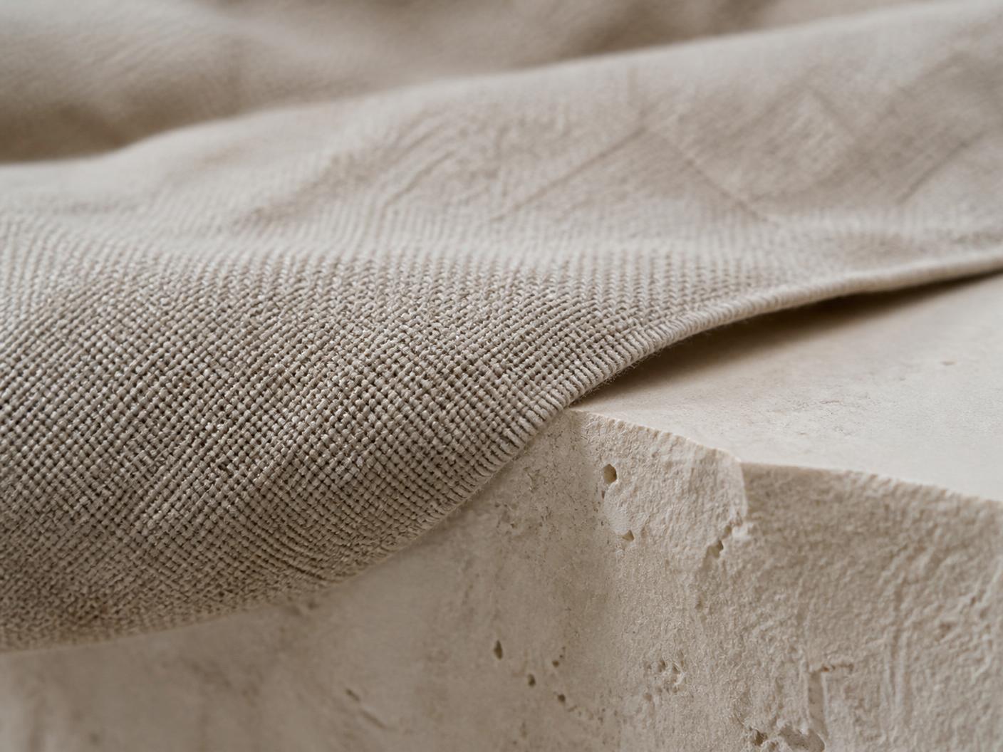 Närbild på otvättat linnetyg draperat över kalkstensskiva